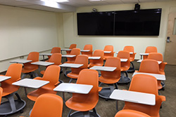 A room of multiple chairs with tablet arms and a large monitor